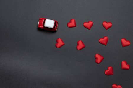 Love delivery. Top view of little children's red toy car with red heart shape on a dark black backgroundの写真素材