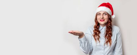 Christmas sale web banner or poster. Beautiful smile woman in Santa Claus hat showing gesture with copy space on a gray background wallの写真素材