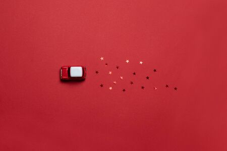 Flat lay of cards with a red model of a childrens car toy with glitter candy on a red saturated background. Holiday delivery idea conceptの写真素材