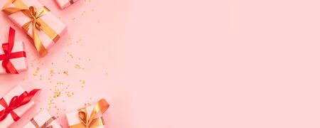 Merry Christmas and Happy New Year greeting card with paper gift box, gold red ribbon bow and glitter confetti on a pink background. Top viewの写真素材