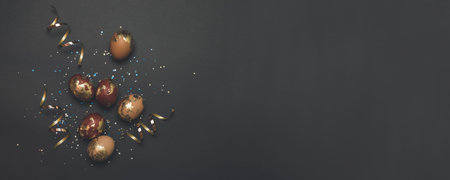 Golden eggs, multicolored shiny sequins, golden glitter serpentine on a dark background with place for text. Can be used for web banner, poster, voucher.の写真素材