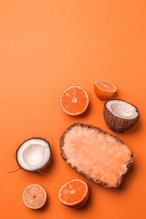 Top view of assorted exotic fruits on an orange background. Pineapple, coconut, orange and lemon half in flat lay style. Vertical photoの写真素材