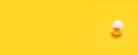 Holiday composition card of white easter egg with love heart decor on yellow background.の写真素材