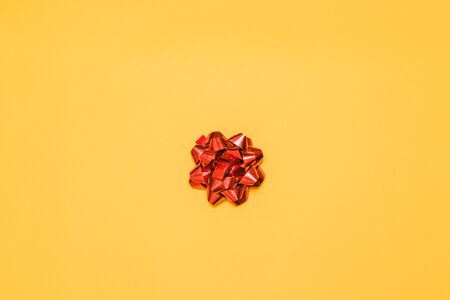 Minimal composition of red shiny bow decor for a gift on yellow background, top view. Greeting cardの写真素材