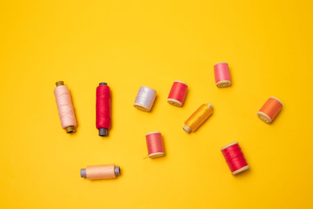 Top view of multi colored thread spools or sewing accessories on a yellow background.