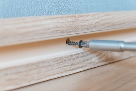 A screwdriver tightens a screw into a light plastic baseboard and wall.Repair in the house.の写真素材