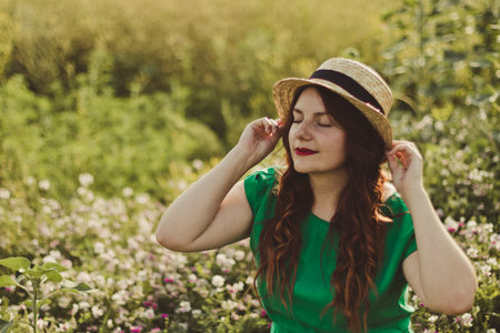 Young curly caucasian girl in a green dress and a straw hat smiles in a flower field on a sunny day. Spring or summer panorama photoの写真素材