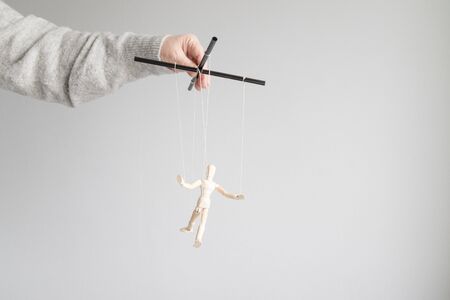Human hand holds a wooden doll on the clothesline on a gray background. Power metaphor conceptの写真素材