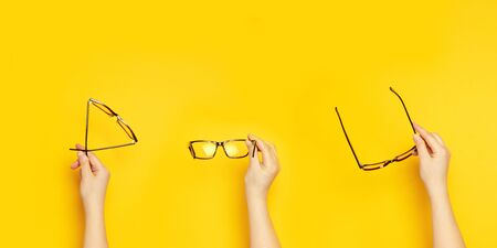 Person hands holds glasses for vision on a yellow background, top view, flat layの写真素材