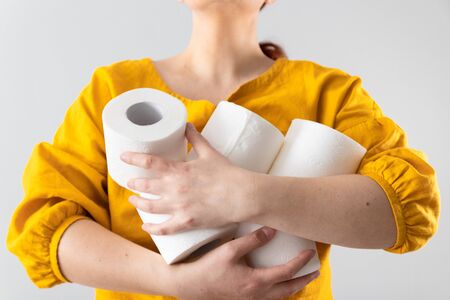 Female hands holds many rolls of toilet paper on a gray wall background in fear of an outbreak of the crown virus closing stores. Buying Essentialsの写真素材