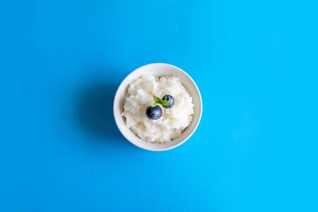 Tasty rice porridge with blueberry berries in a white bowl on blue background. Proper healthy eating breakfast concept.の写真素材