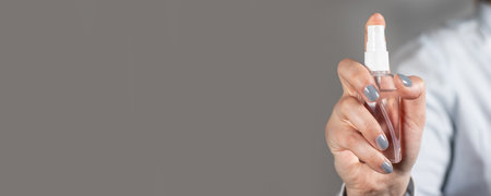 Female hand holds a plastic bottle with a sanitizer spray on a gray background removed. A tool for...