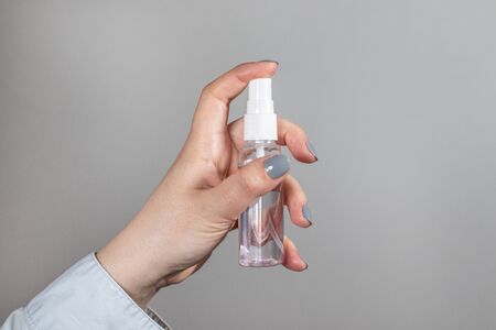 Female hand holds a plastic bottle with a sanitizer spray on a gray background removed. A tool for protection against coronavirus, pandemicの写真素材