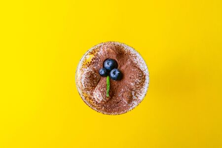 Top view of tiramisu dessert with mint and strawberries in a glass on a yellow backgroundの写真素材