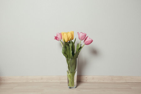 Beautiful yellow and pink tulips in a glass vase on the floor in the room