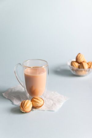 Hot coffee with milk in a glass cup and cookies on a blue background. Vertical photoの写真素材