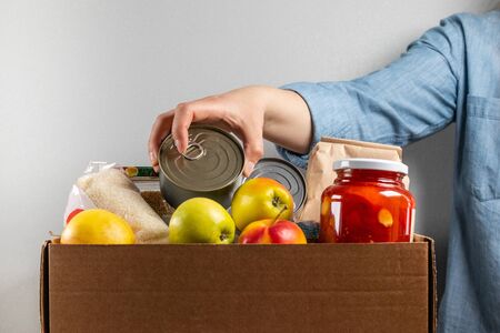 Female hand puts tin can in food donation boxの写真素材