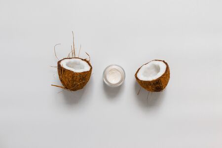 Cosmetic cream for face or body in a glass jar with half a coconut on gray background, top view, flat layの写真素材