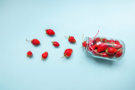 Flatlay composition of juicy selected strawberries in a glass bottle.