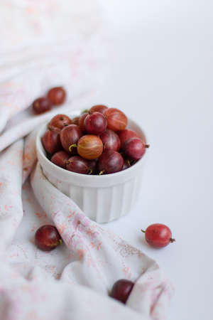 Fresh gooseberries in a ceramic bowl on white table. View from above. Vertical photoの写真素材