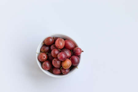 Fresh gooseberries in a ceramic bowl on white table. View from above.の写真素材