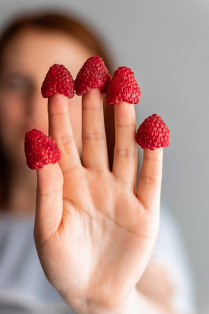 Young girl with raspberry berries on the fingers, focus on hands