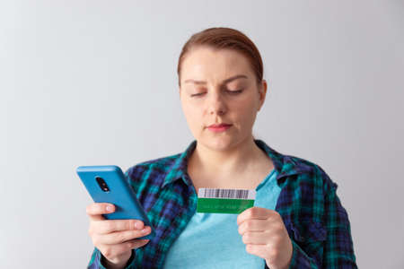 Beautiful young woman online shopping with credit card and smartphone sitting at home. Contactless payment conceptの写真素材