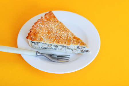 Quiche pie with spinach and chicken on white plate on yellow background