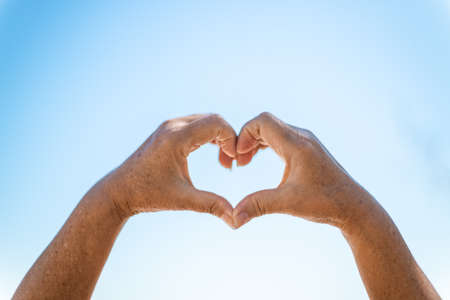 Woman making heart with her hands on blurred blue backgroundの写真素材
