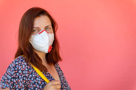 Portrait of young red hair girl in a protective medical mask on a pink wall background. Coronavirus, covid 19 conceptの写真素材