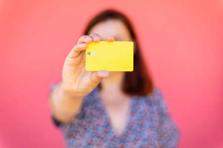 Pretty happy woman showing blank plastic card, stands near a pink wall in the streetの写真素材