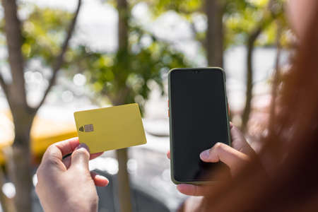 Woman holding a credit card using mobile phone on the street. Online shopping conceptの写真素材