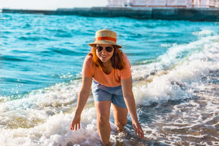 Smiling red-haired girl in hat, shorts and t-shirt looking at the camera at the sea. Travel and vacation concept.の写真素材