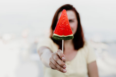 Girl holding a lollipop in the form of a watermelon in the summer by the sea