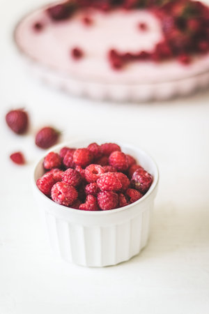 Fresh large raspberries in a white mask and a pie on the background, vertical photo