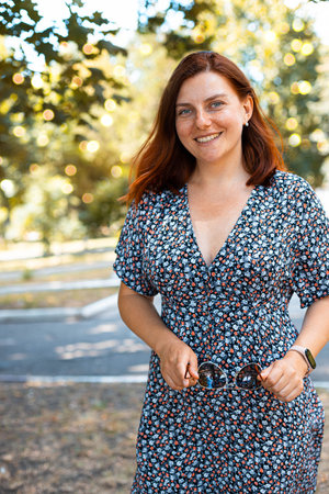 Vertical photo of cute red-haired girl in smiling and looking at the camera in the park