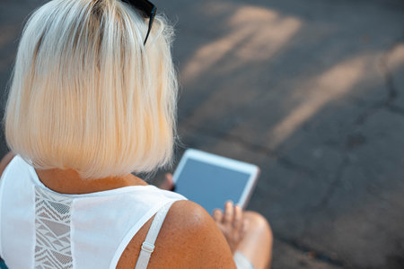 Freelancer blonde woman uses digital tablet device working in the park in summer