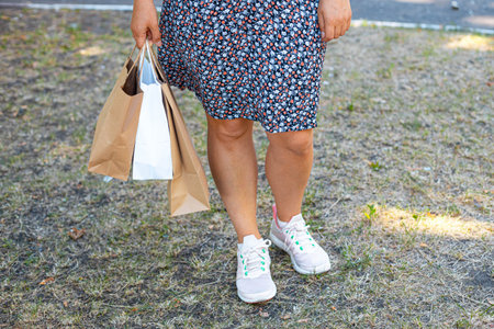 Female hand holding paper shopping bags in the park on the street. Clearance shopping concept