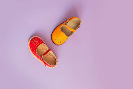 Bright yellow and red kids shoes on a lilac background with copyspace. Baby clothes concept. Top view, flat layの写真素材
