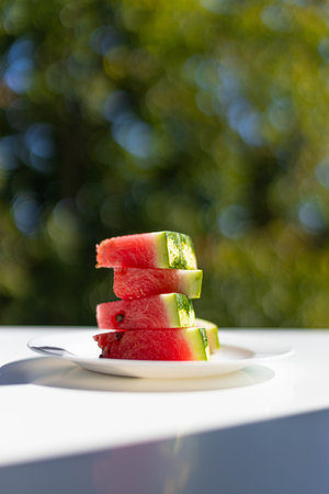 Ripe slices of watermelon on a white plate. Vertical orientation photo with green blurred background