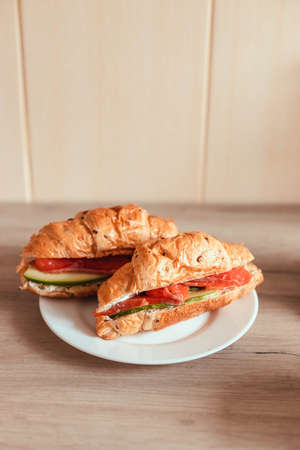 Fresh french croissant with salmon and cucumber on a plate on a wooden table. Vertical photo orientationの写真素材
