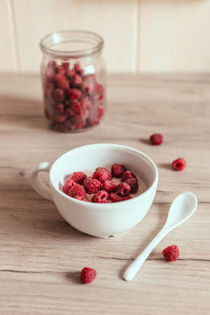 Fresh homemade oatmeal with raspberries in a bowl on the table in the kitchen. Delicious breakfast. Vertical photo orientationの写真素材