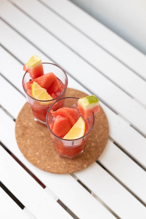Watermelon smoothie in glass jars with sliced fruit on white wooden table