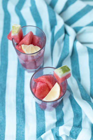 Glass jar with watermelon pulp cocktail on striped towel on white wooden board. Vertical orientationの写真素材