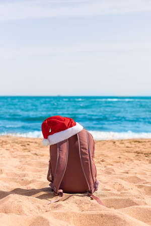 Santa hat on a sports backpack lying on the beach of the sea coast. Vertical orientation of the photoの写真素材