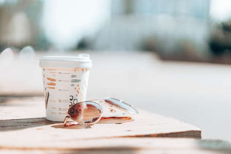 A cup of hot coffee with sunglasses on a wooden tableの写真素材