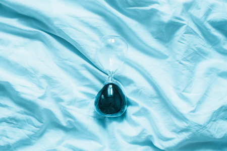 Transparent hourglass on blue bed with copyspace