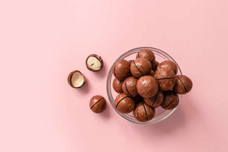 Raw macadamia nuts in a transparent glass bowl on pink solid background. Minimal composition.の写真素材