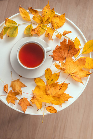 Cup of tea on wooden coffee table with yellow fall leaves. Comfort and relaxation concept, vertical...