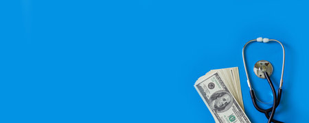 Stethoscope and 100 dollar bills on blue background with copy space. Top view. Medical banner for...